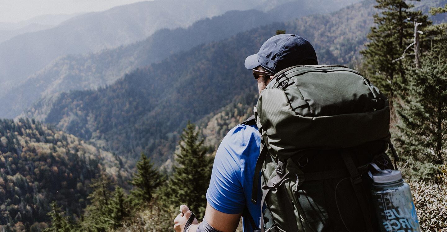 man with a hiking backpack on walking through the woods during daytime