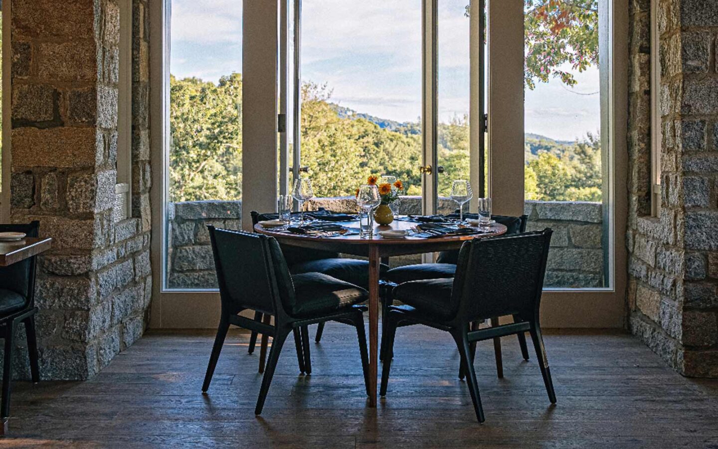 dining table and chairs in an industrial style dining room with large windows overlooking the forest