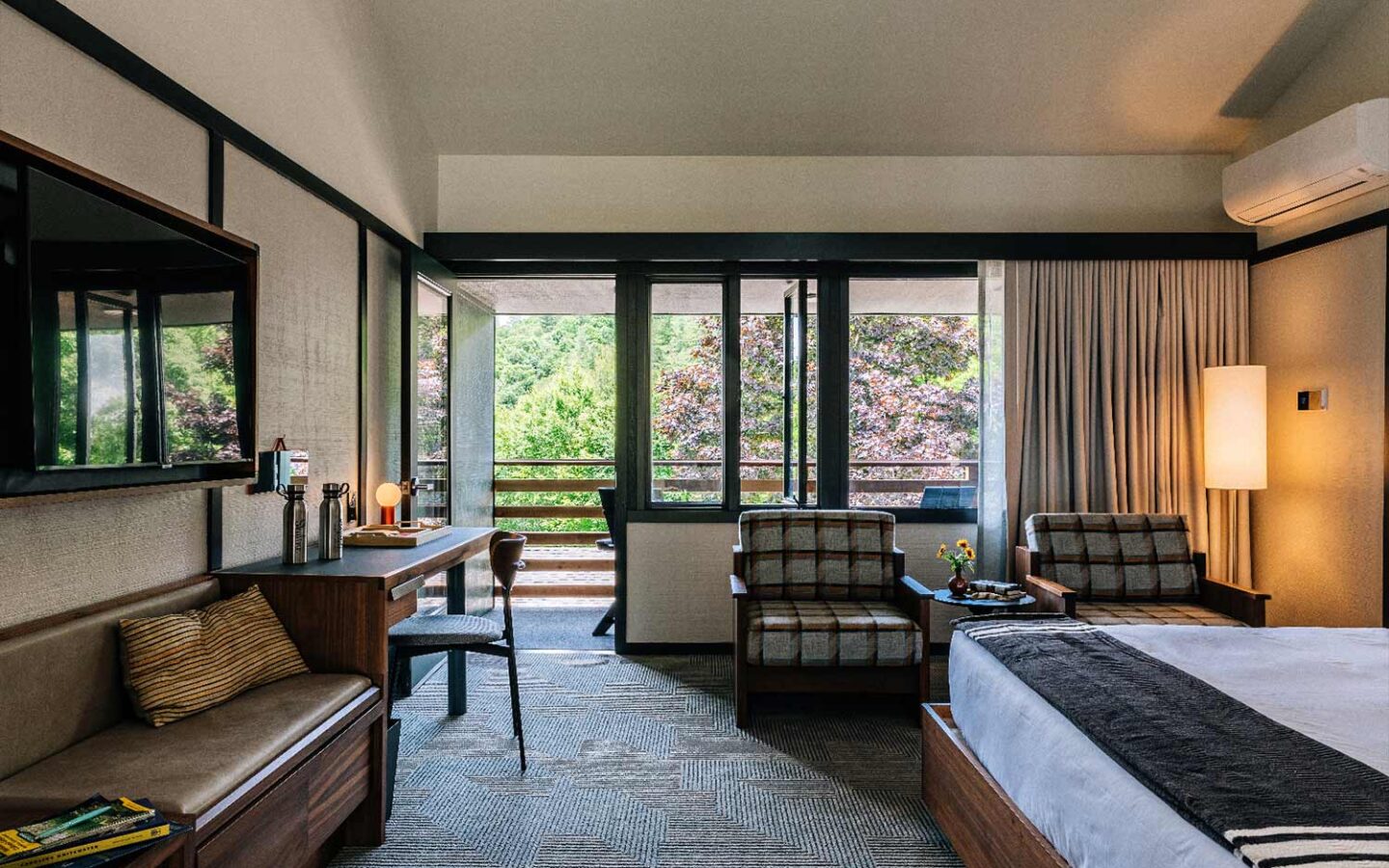 lodge guest room with a large bed, tv with two reading couches and balcony