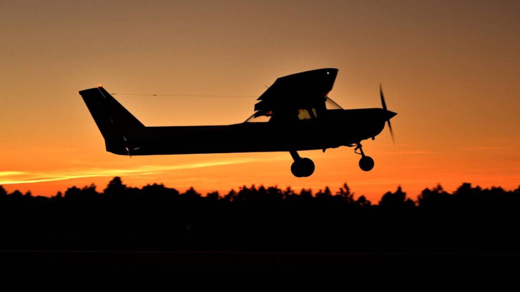 fixed wing airplane flying over tree tops at sundown